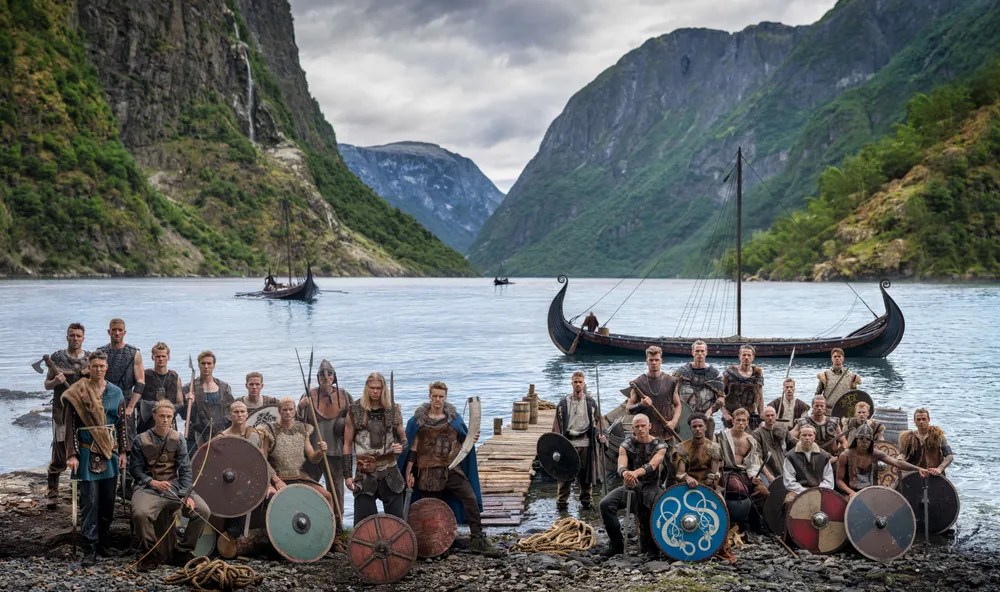 Norway's football team dressed as Vikings lined up in front of a longship in a Norwegian fjord